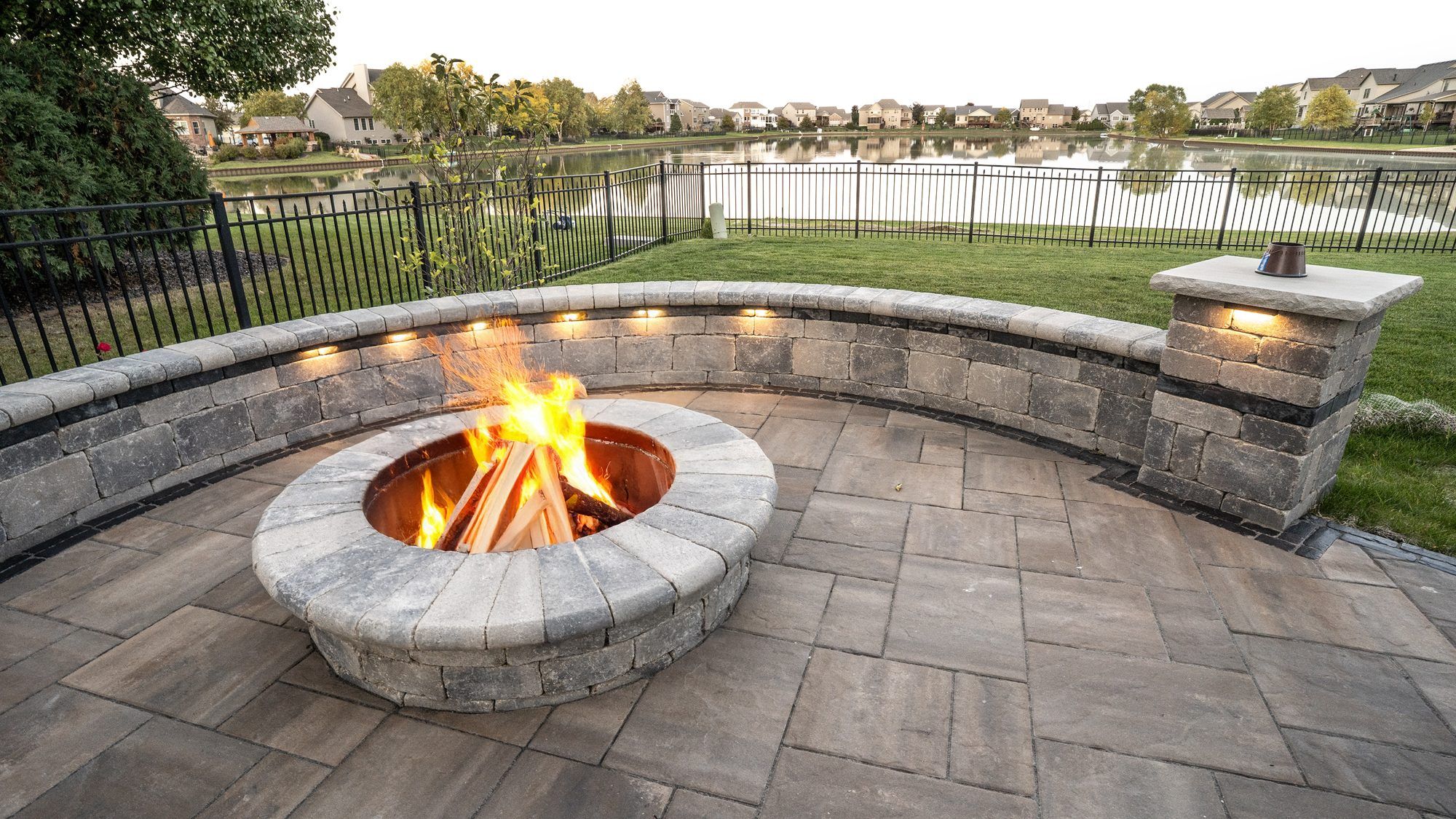 Wood-burning fire pit with a lit seat wall overlooking a pond