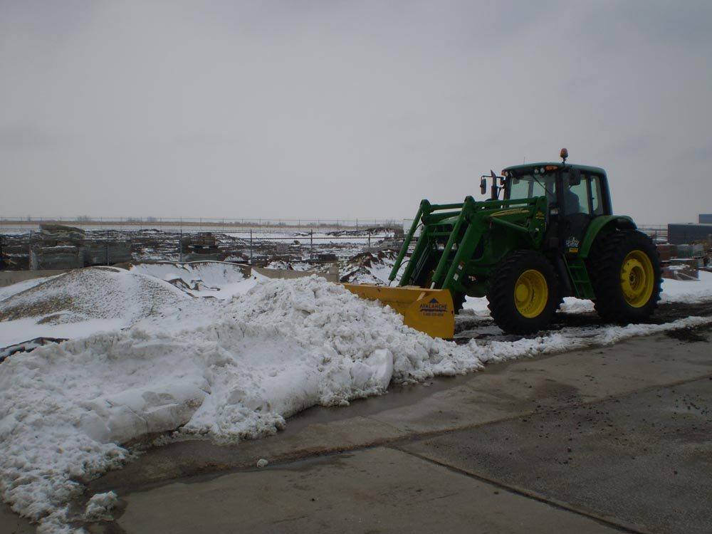 F&W tractor with a loader bucket stacking snow on a commercial lot