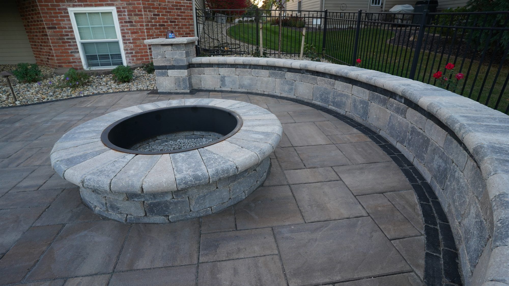Round stone fire pit inside a curved seat wall on a paver patio