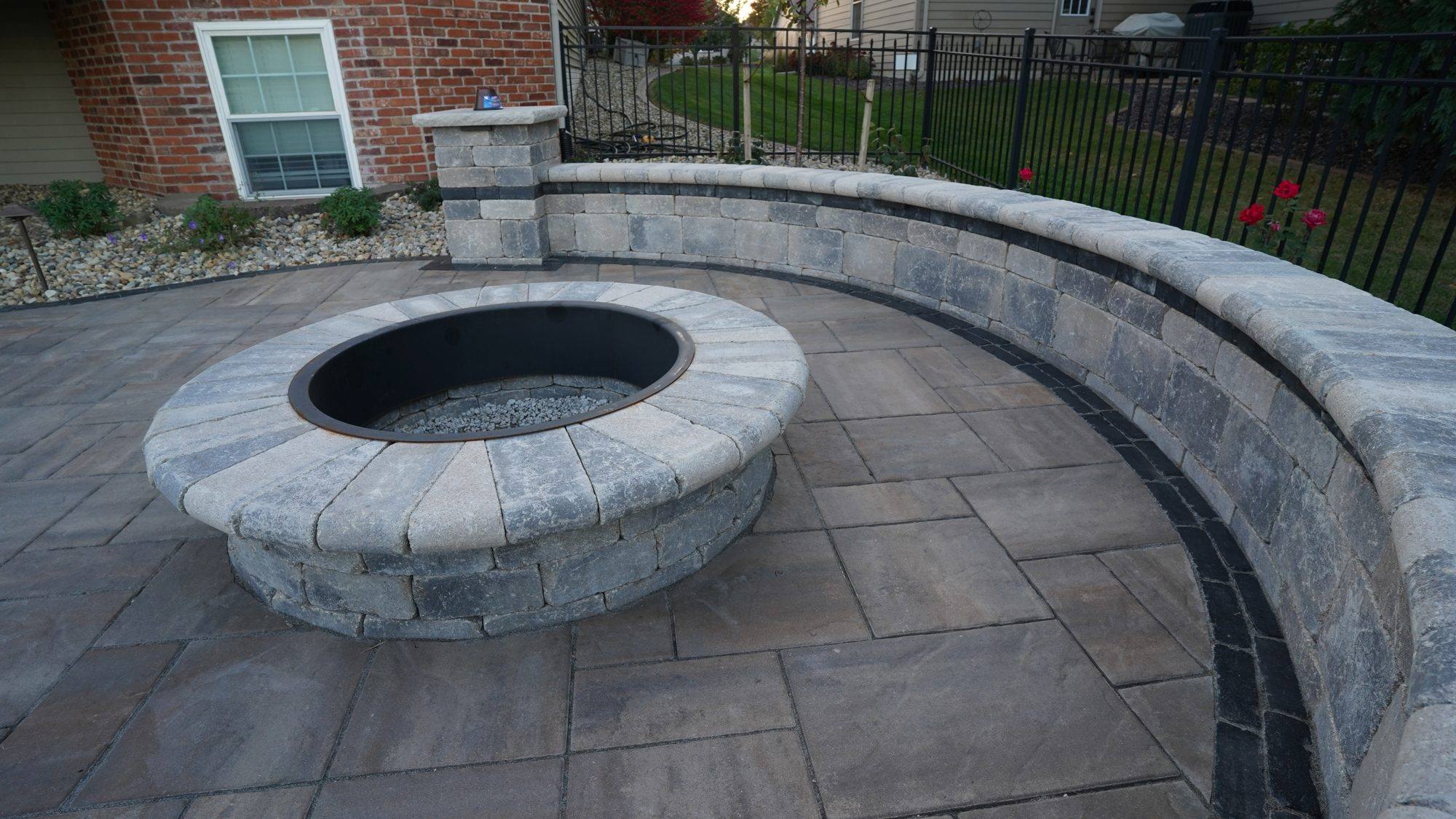 Round stone fire pit inside a curved seat wall on a paver patio
